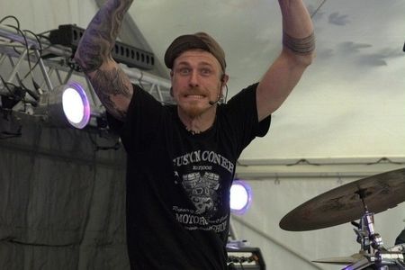 Schlagzeuger schaut in die Kamera und hält seine Drumsticks hoch